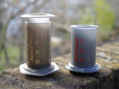 Two assembled AeroPress coffee makers on stone wall